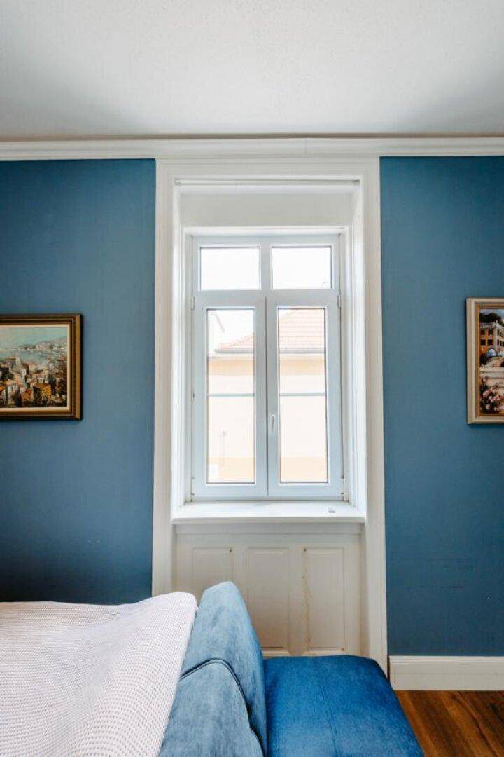Helles Fenster in einem Schlafzimmer mit blauen Wänden und weißem Rahmen.