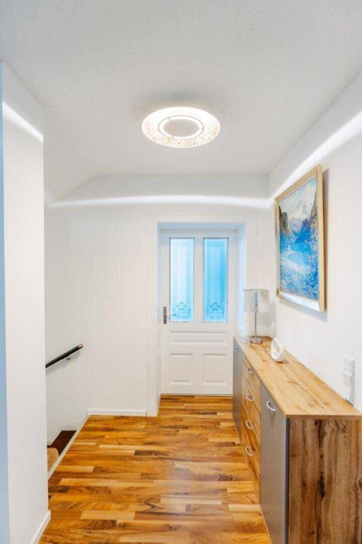 Heller Flur mit Holzboden, moderner Kommode und einer Tür am Ende des Ganges.