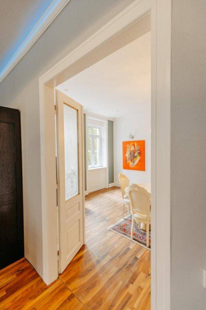 Blick durch eine offene Tür in ein elegantes Esszimmer mit weißem Esstisch und Stühlen.