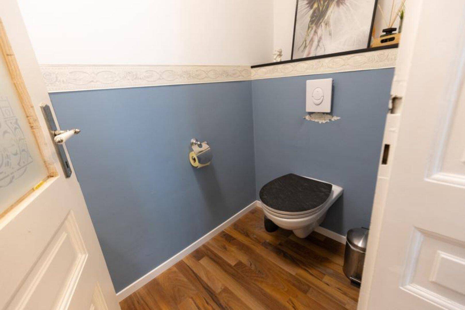 Modernes Gäste-WC mit blauen Wänden, Holzboden und wandhängendem WC.