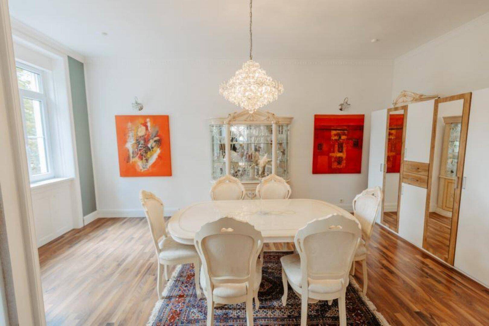 Elegantes Esszimmer mit großem ovalen Tisch, Kronleuchter und Vitrinen im klassischen Stil.