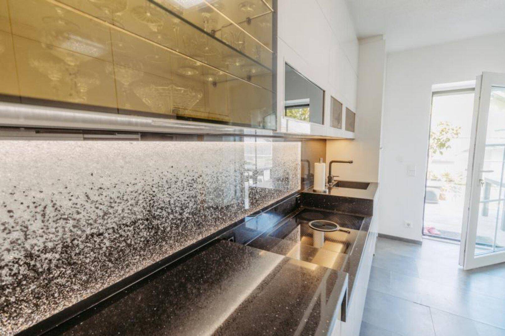 Moderne Küche mit weißen Schränken, schwarzen Arbeitsplatten und Ausgang zur Terrasse.