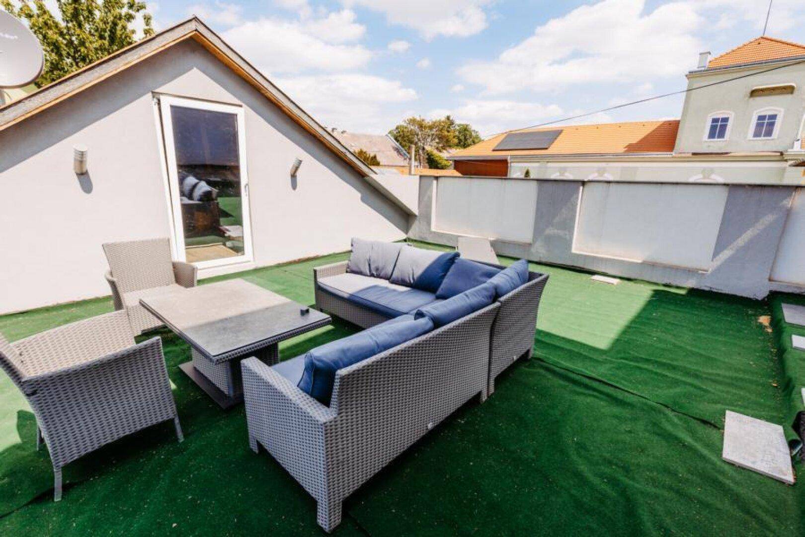 Dachterrasse mit Kunstrasen, bequemen Outdoor-Möbeln und Zugang zum Innenbereich.