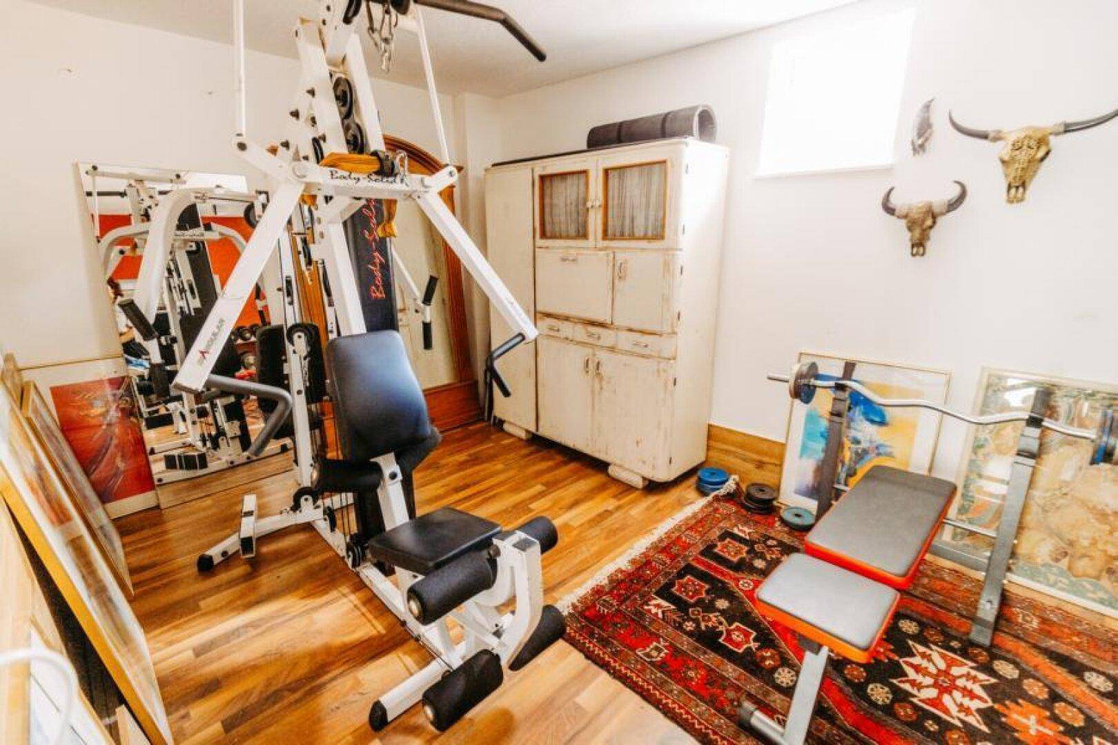 Geräumiger Fitnessraum mit verschiedenen Trainingsgeräten und Holzboden für das tägliche Workout.