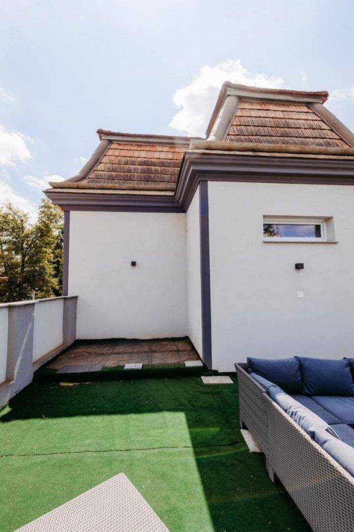 Blick von der Dachterrasse mit Kunstrasen und Outdoor-Möbeln auf das Gebäude.