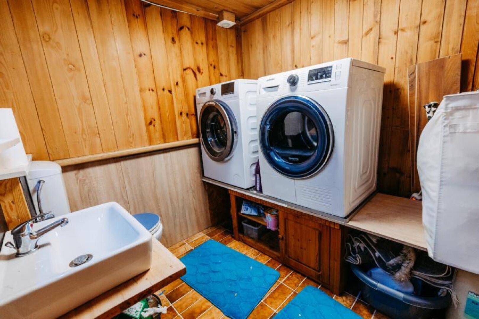 Praktischer Hauswirtschaftsraum mit Waschmaschine, Trockner, Waschbecken und Holzverkleidung.