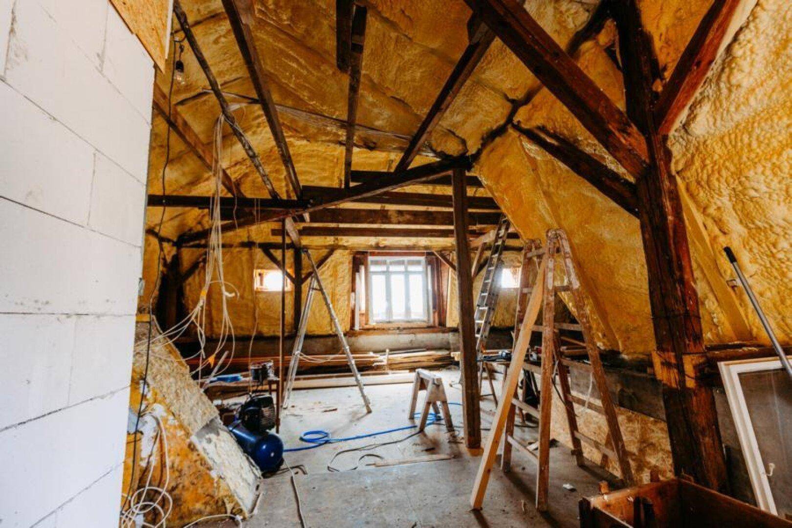 Dachboden im Umbau mit sichtbaren Holzbalken, Isolierung und Baugeräten.
