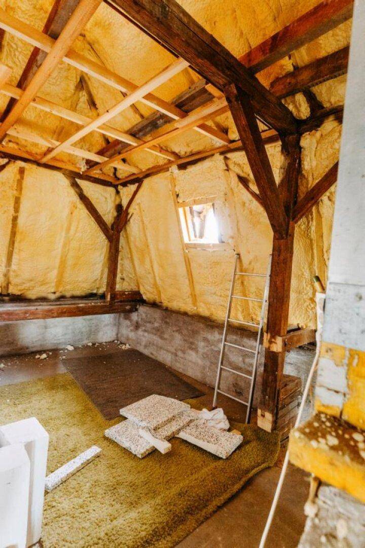 Teil des Dachbodens mit Holzbalken, Isolierung und einem kleinen Fenster.