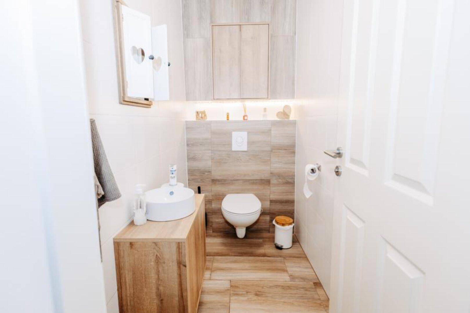 Modernes Gäste-WC mit wandhängender Toilette, Aufsatzwaschbecken und Holzdetails.