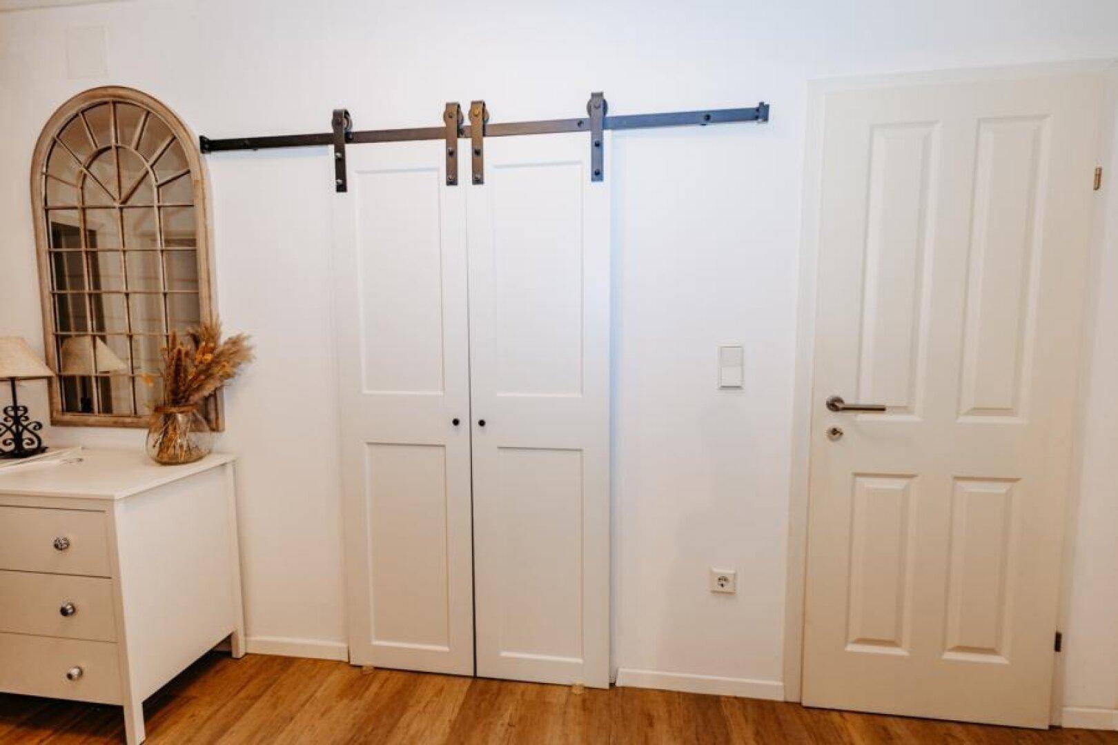 Heller Flur mit Schiebetür, großem Spiegel und Kommode im modernen Landhausstil.