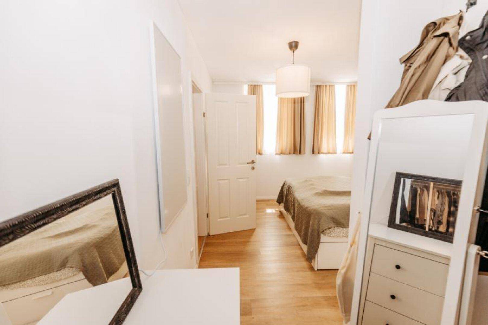 Helles Schlafzimmer mit Doppelbett, Spiegeln und Kommode.