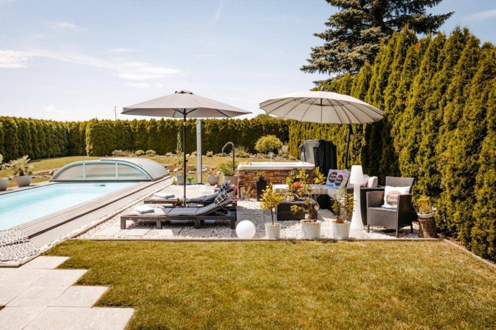 Entspannungsbereich im Garten mit Whirlpool, Liegestühlen und Sonnenschirmen unter blauem Himmel.