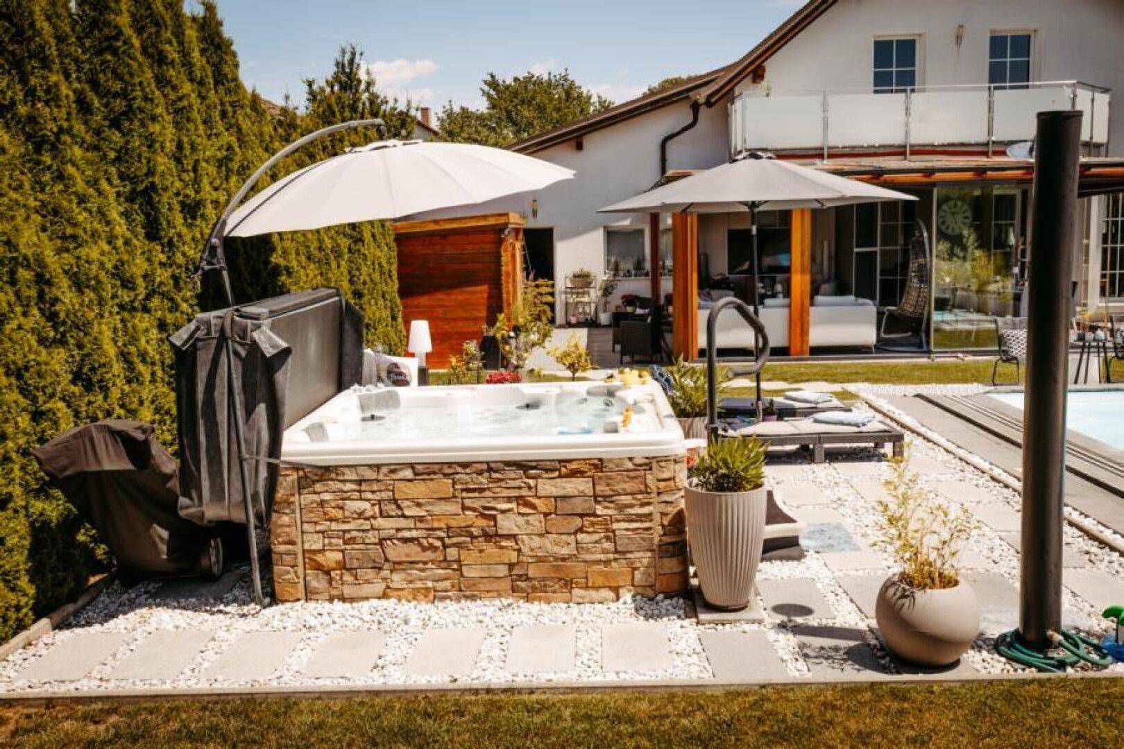 Detailansicht des luxuriösen Whirlpools im Garten, umgeben von Steinverkleidung und Pflanzen.