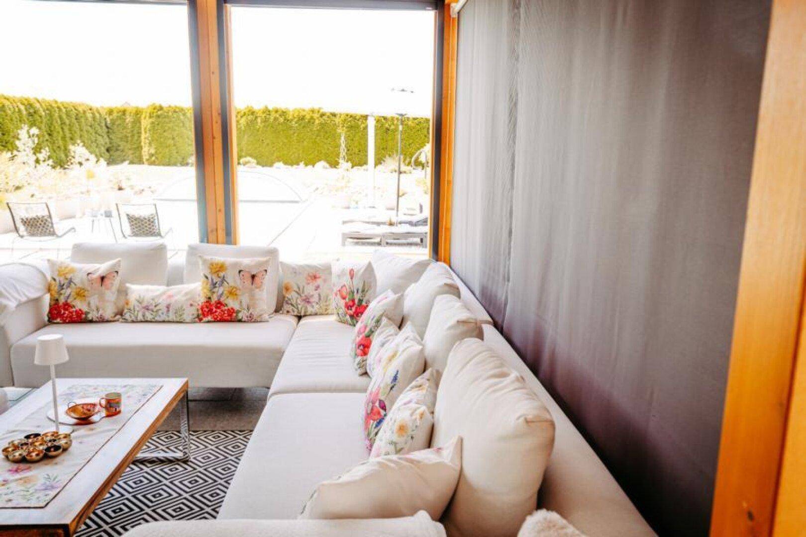 Heller Wintergarten mit großem Ecksofa und weitem Blick auf den gepflegten Garten und Poolbereich.