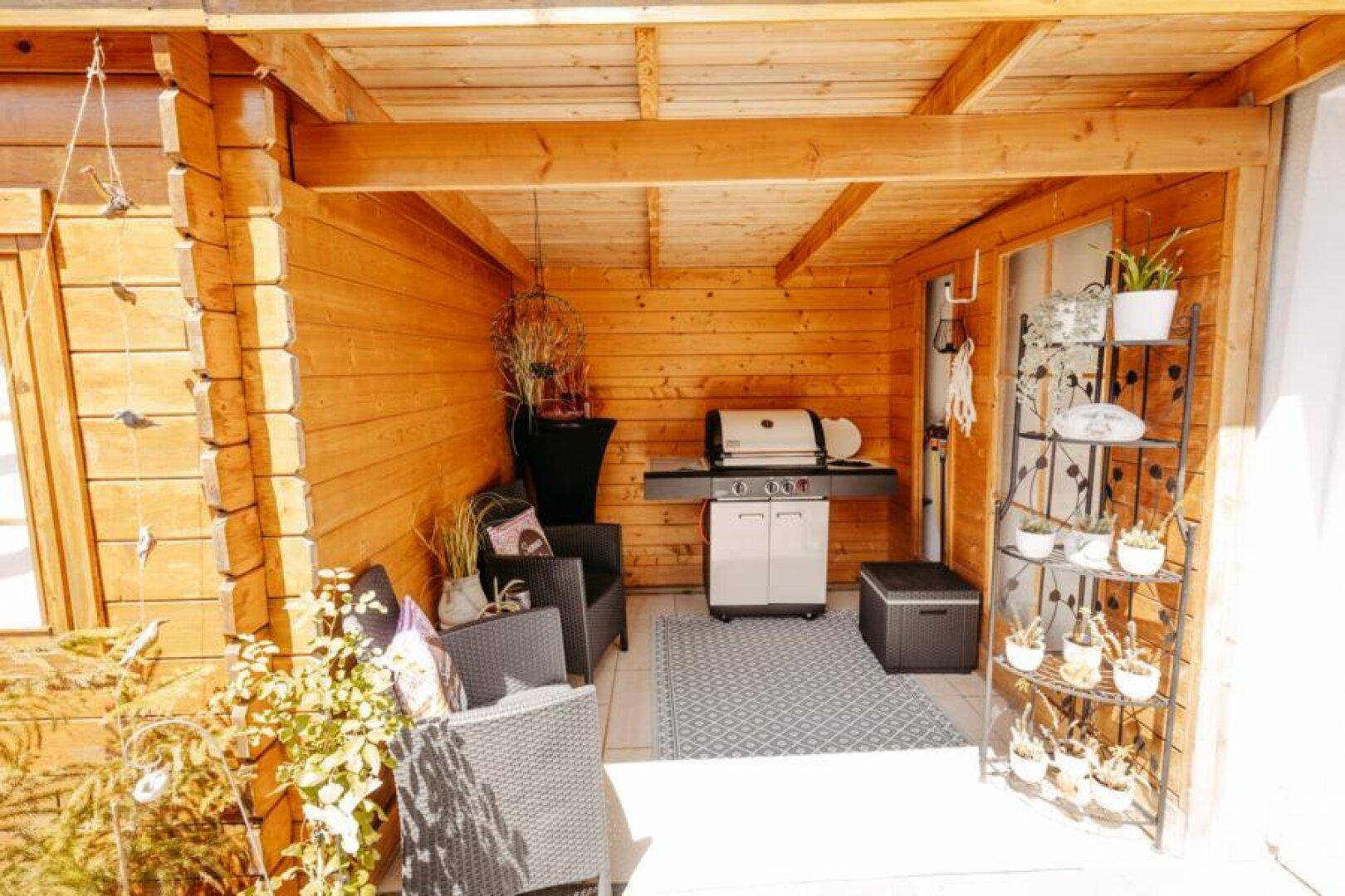 Überdachter Außenbereich mit Holzverkleidung, Grillstation und gemütlicher Sitzecke für gesellige Abende.