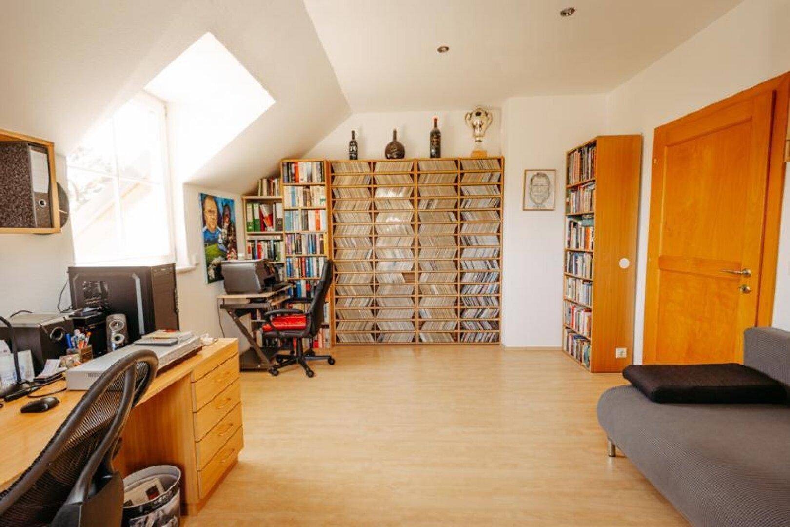 Geräumiges Arbeitszimmer mit umfangreichen Bücherregalen, Schreibtisch und einem Dachfenster.