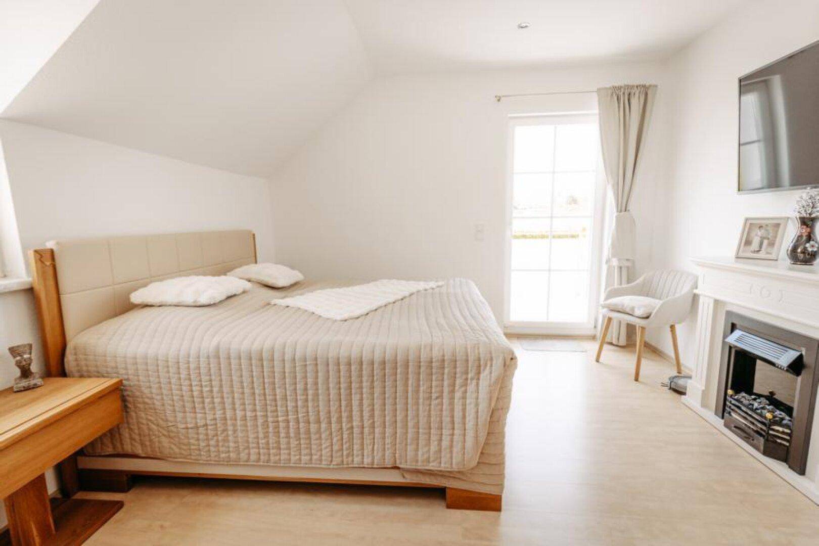 Gemütliches Schlafzimmer mit Doppelbett, Holzboden und Zugang zu einem Balkon.