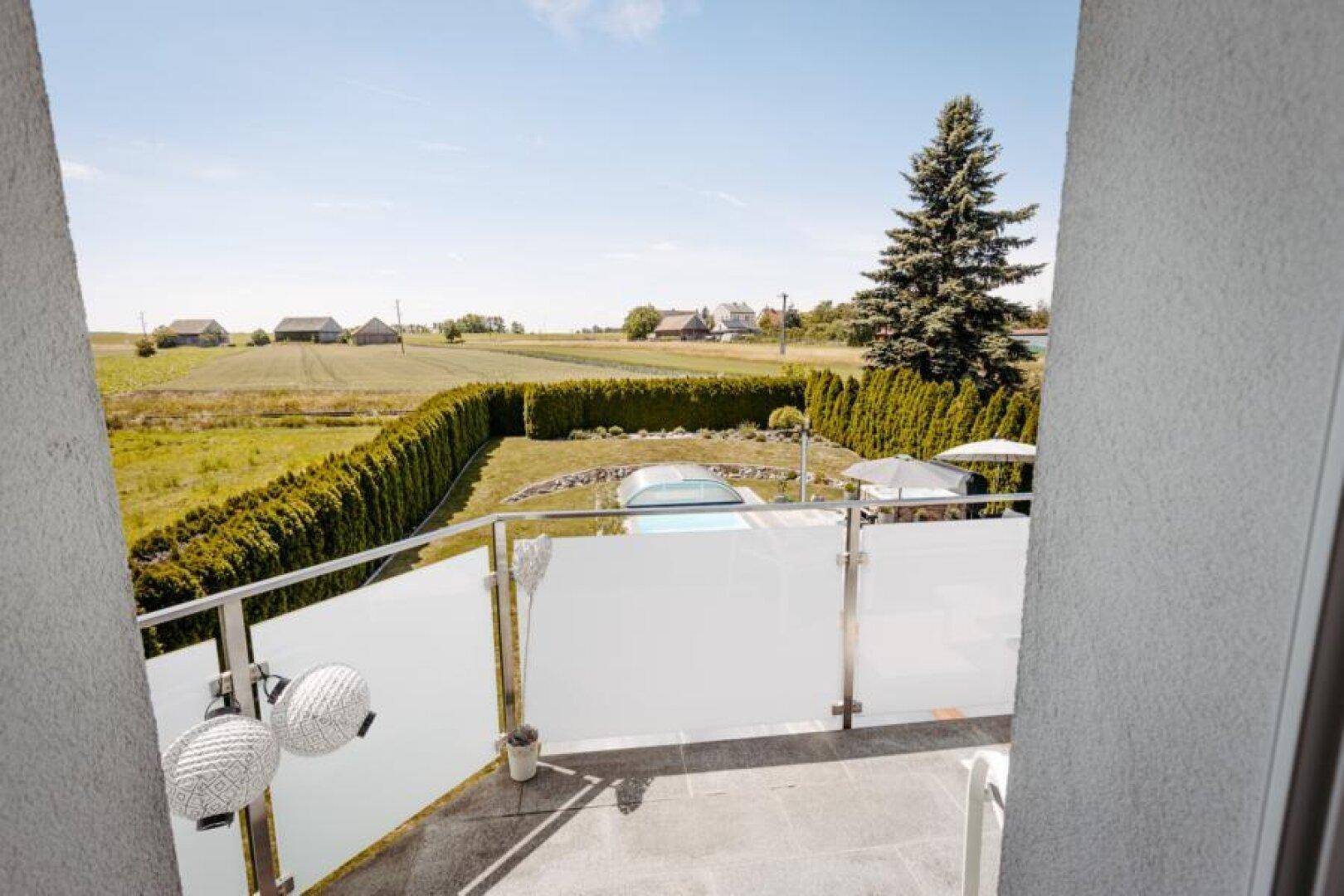 Balkon mit weitem Blick über grüne Felder und einen Garten mit Pool.