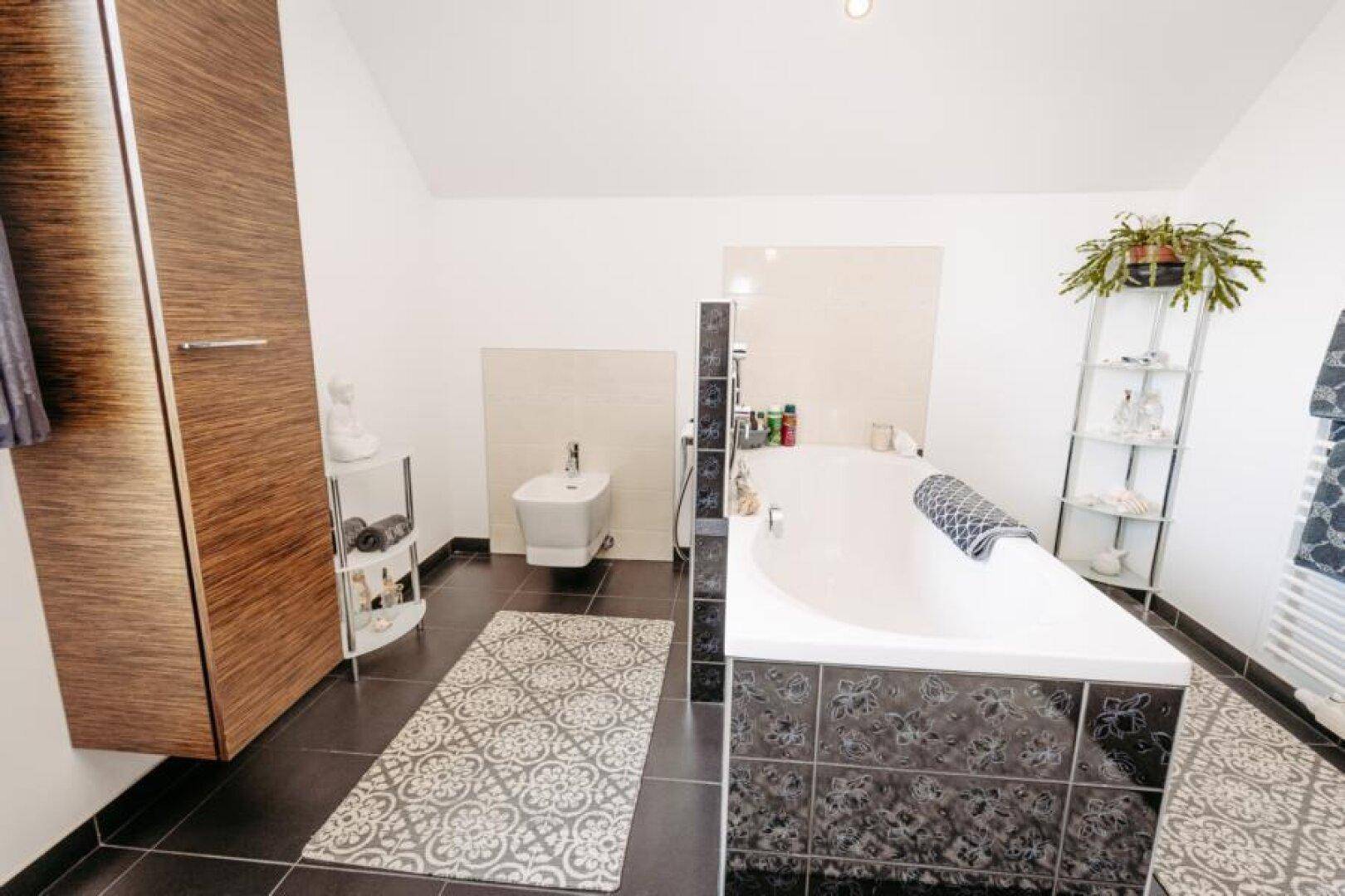 Geräumiges Badezimmer mit Badewanne, Bidet und dunklen Fliesen.