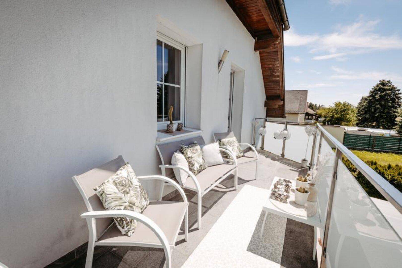 Heller Balkon mit bequemen Sitzgelegenheiten und Blick ins Grüne.