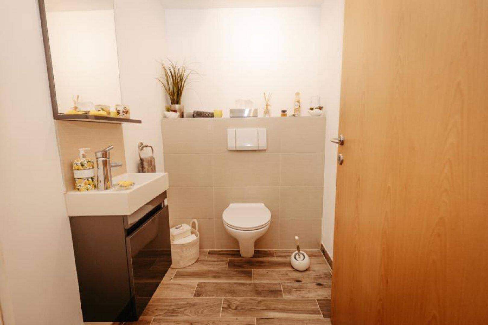 Modernes Gäste-WC mit Wand-WC, kleinem Waschbecken und Holzoptikfliesen.
