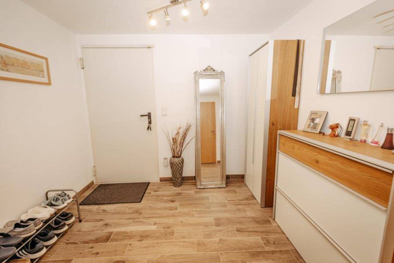 Heller Flur mit Holzoptikfliesen, Garderobe und großem Spiegel.