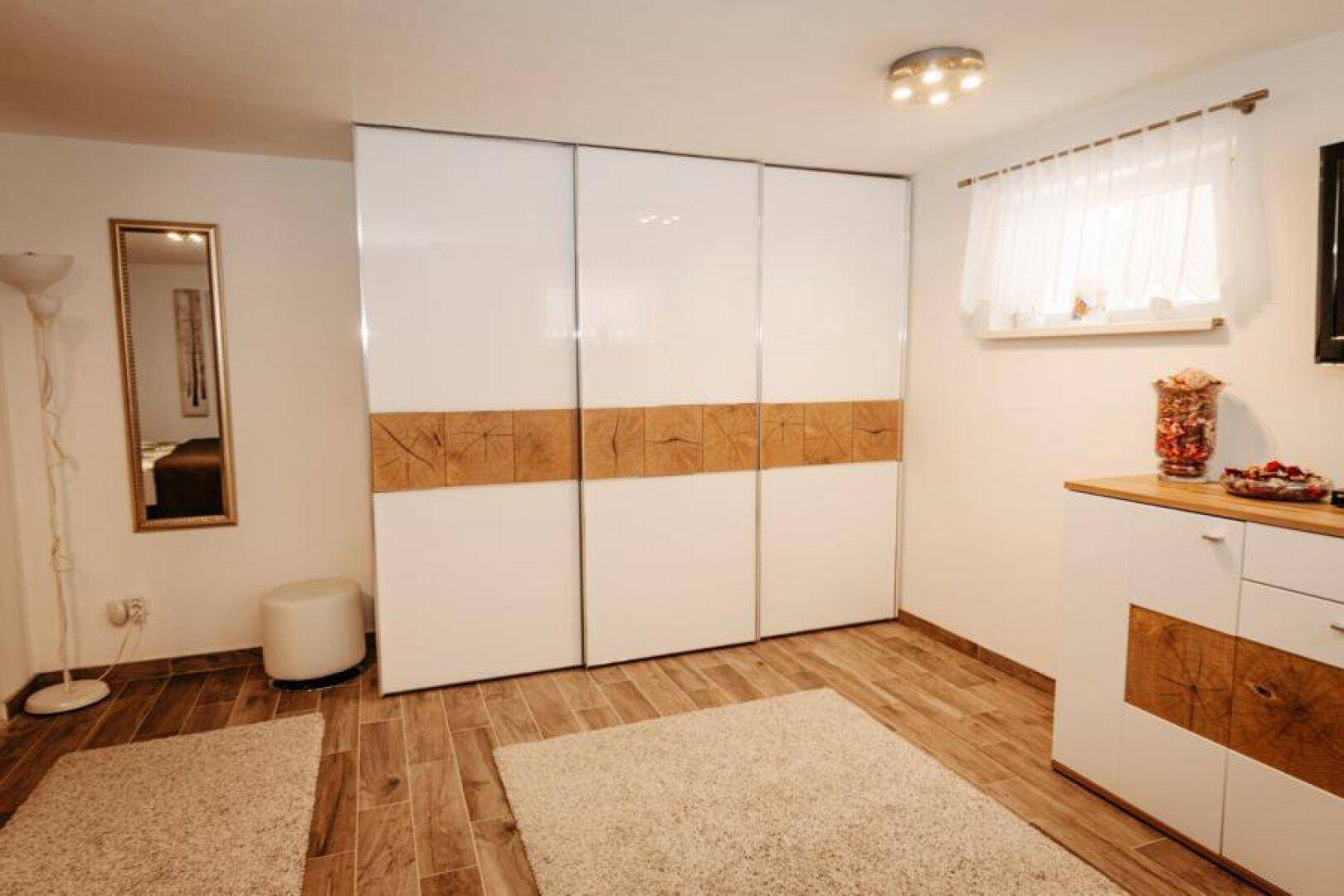Schlafzimmer mit großem Kleiderschrank, Holzoptikfliesen und Fenster.