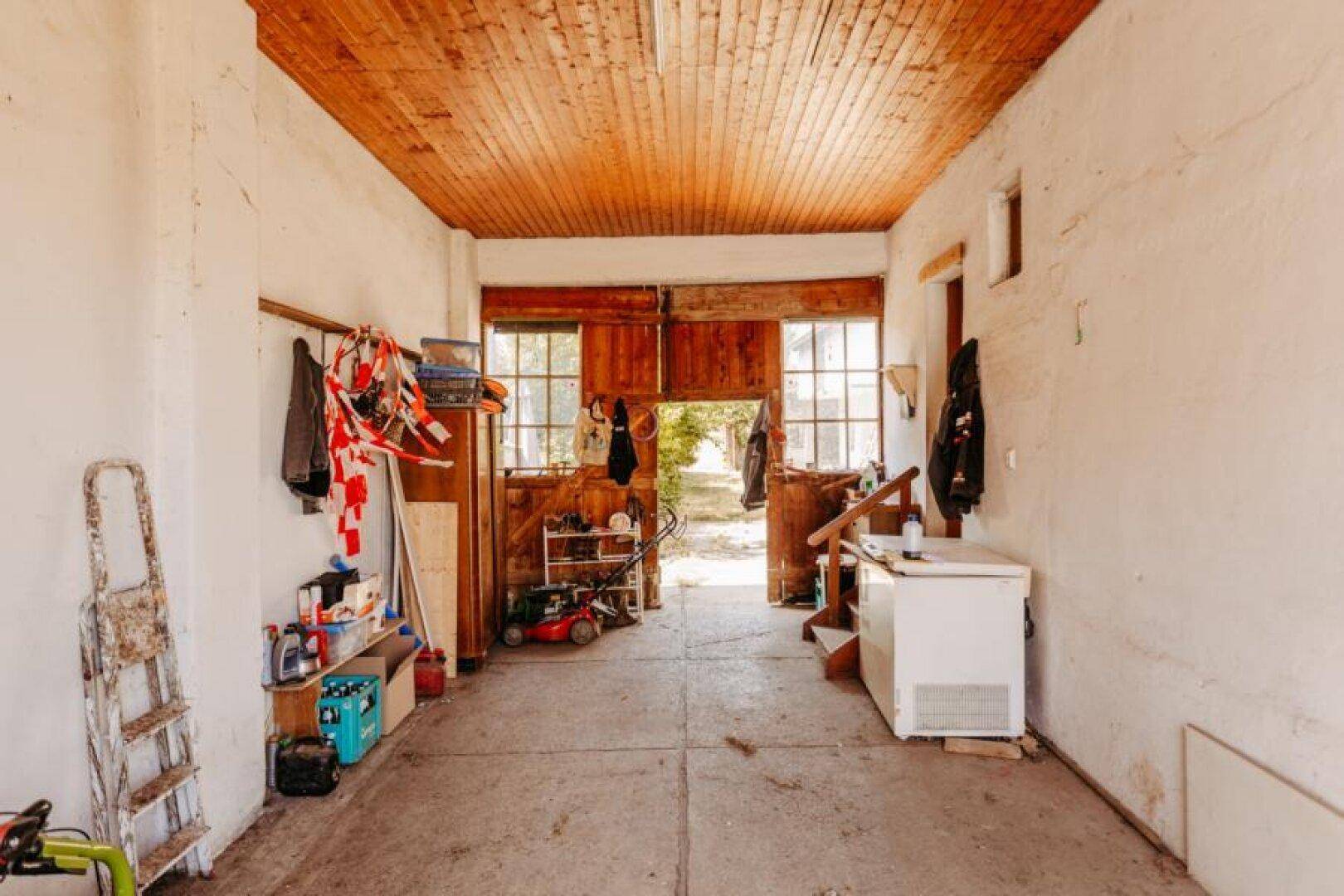 Geräumige Garage mit Holzbalkendecke, Betonboden und Blick ins Freie durch große Holztüren.