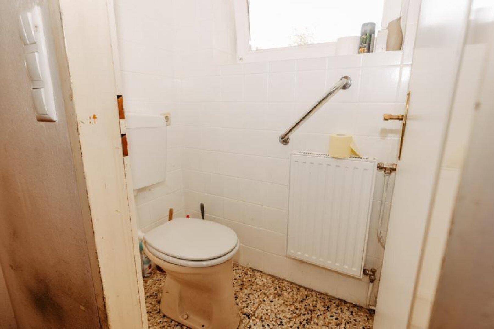 Kleines WC mit weißen Fliesen, Toilette und Haltegriff für Barrierefreiheit.