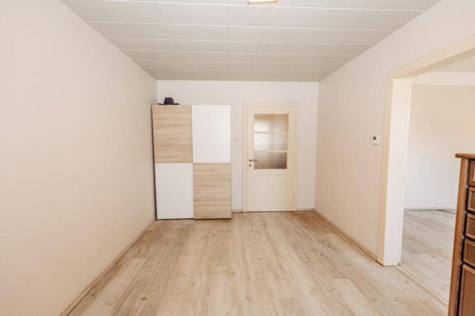 Geräumiges Zimmer mit Laminatboden, weiß gestrichenen Wänden und einem modernen Schrank.