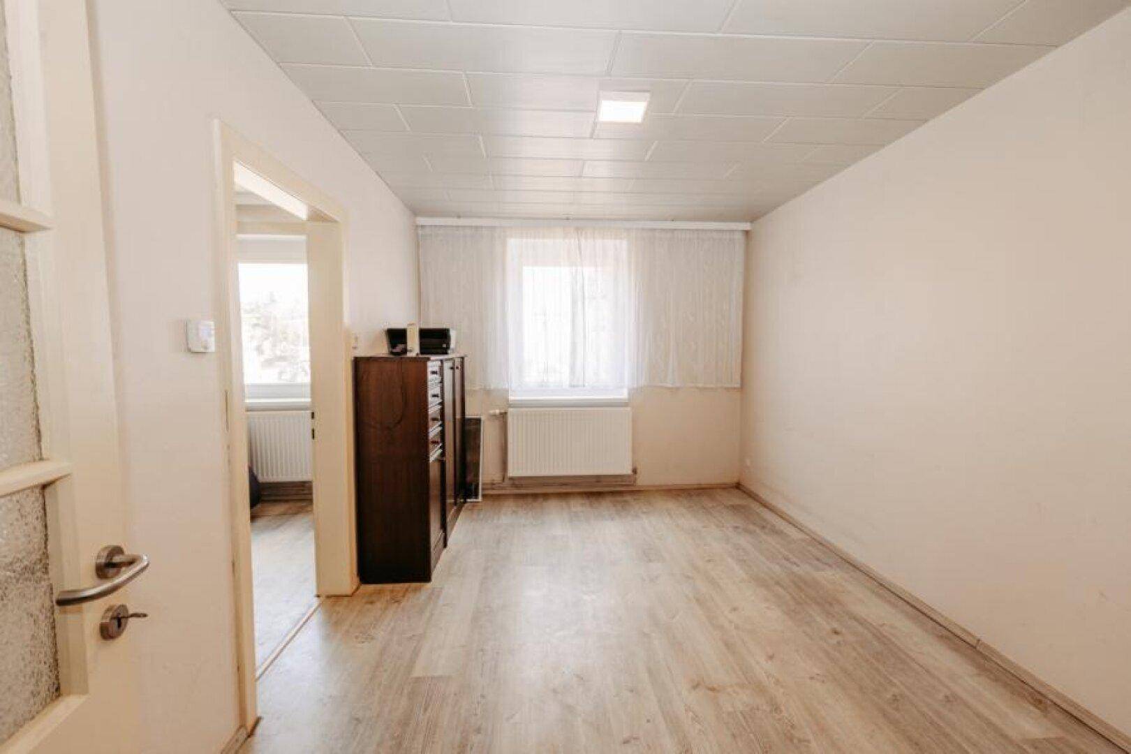 Helles, leeres Zimmer mit Laminatboden und Fenster, bereit zur individuellen Gestaltung.