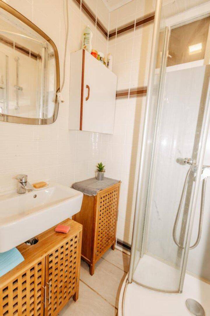Badezimmer mit Duschkabine, Waschbecken und Holzunterschränken in hellem Ambiente.