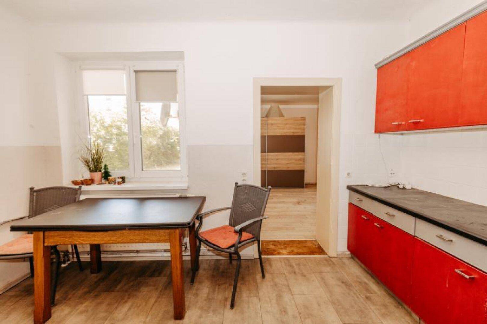 Küche mit roter Einbauküche, Esstisch und Fenster, bereit für Mahlzeiten.