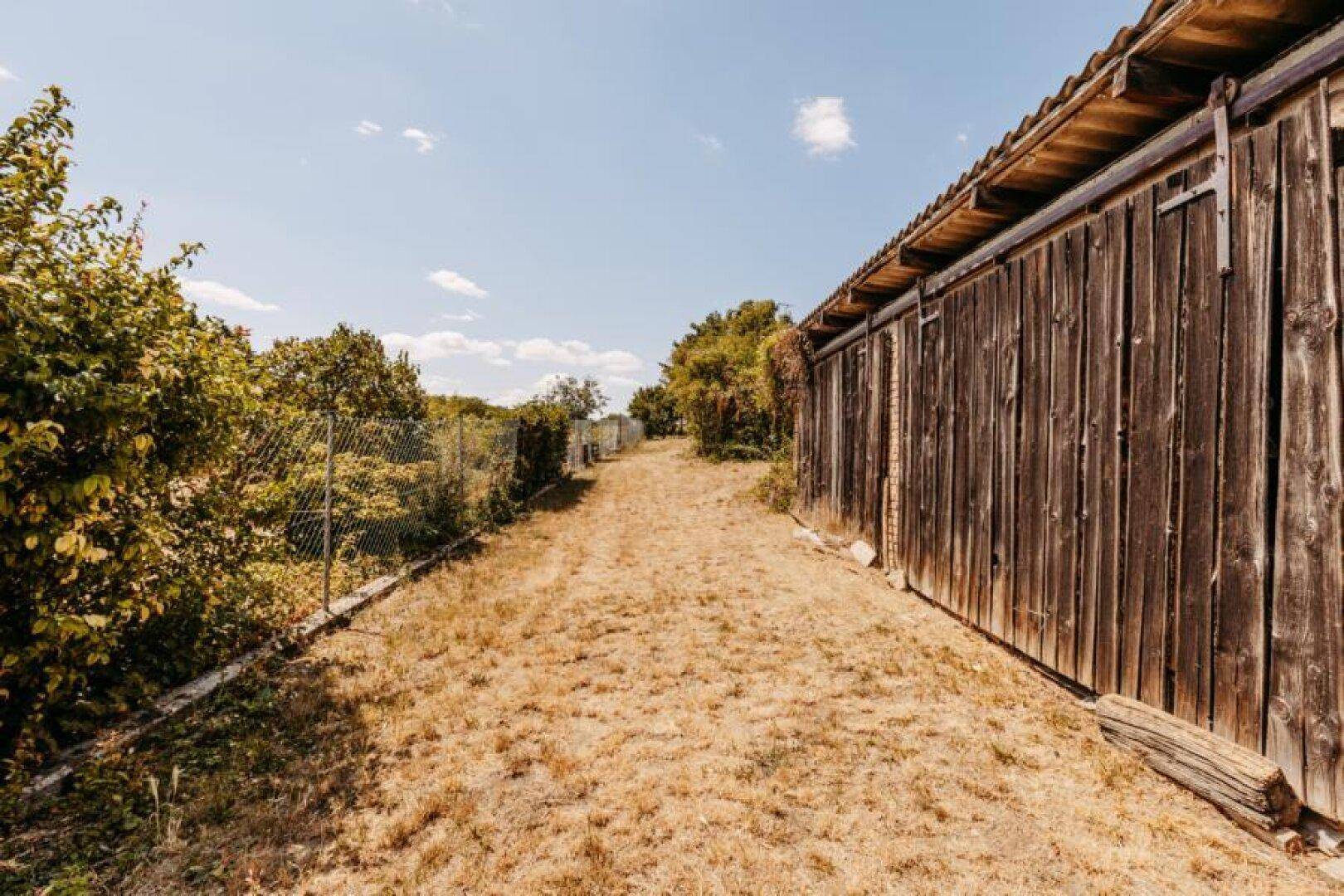 Langer, unbefestigter Weg entlang einer Holzscheune unter blauem Himmel.