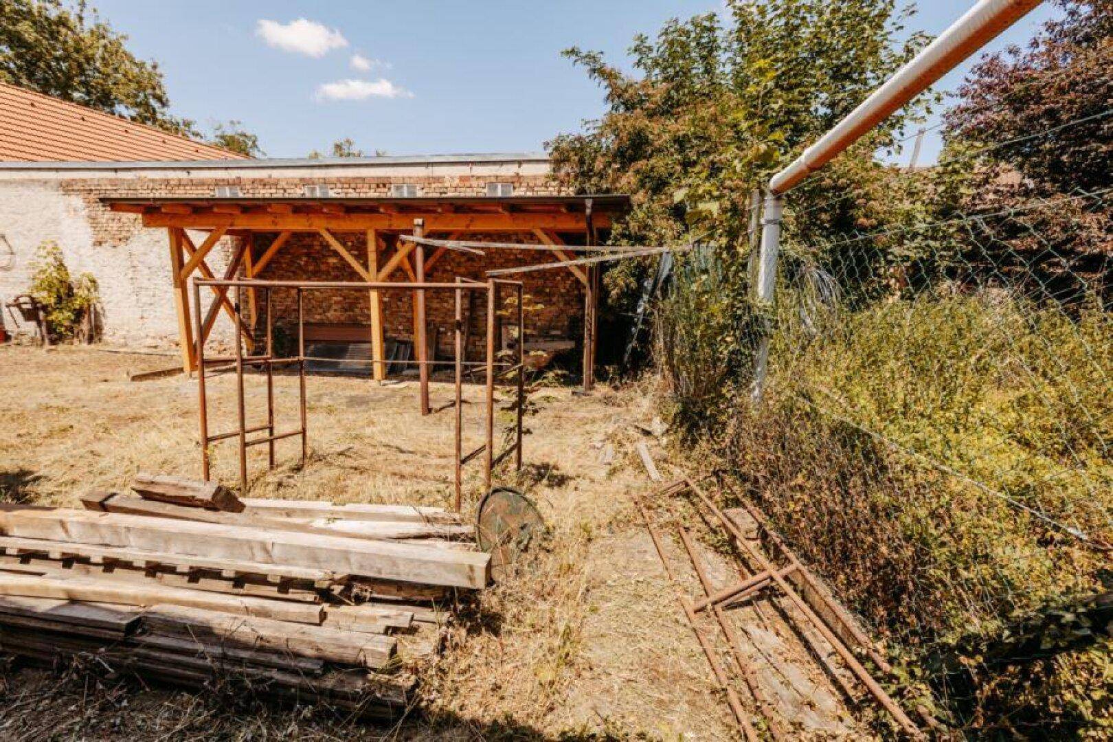 Verwilderter Gartenbereich mit einer Holzüberdachung und viel Grün.