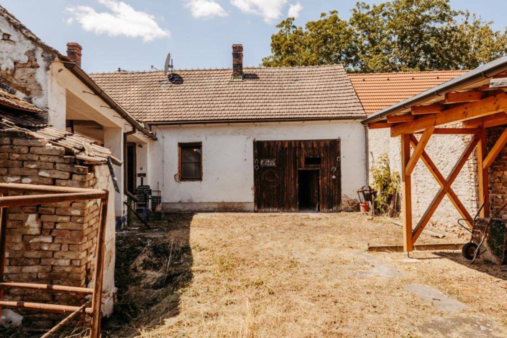 Hinterhofansicht des Hauses mit Nebengebäuden und trockenem Rasen.