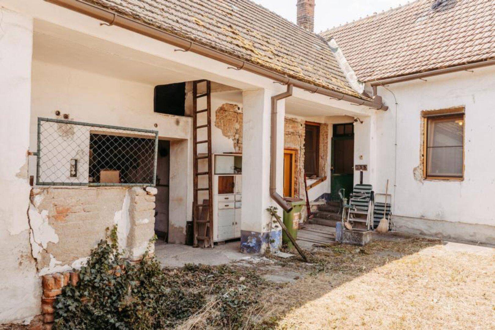 Innenhof mit alten Gebäudestrukturen, verputzten Wänden und einer Holzleiter.