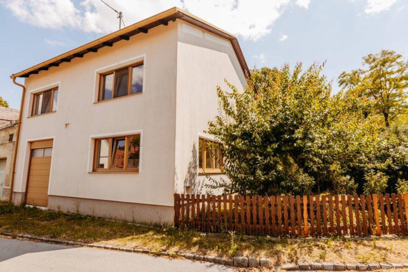 Vorderansicht eines Hauses mit Garage und Holzzaun, umgeben von Grünflächen.
