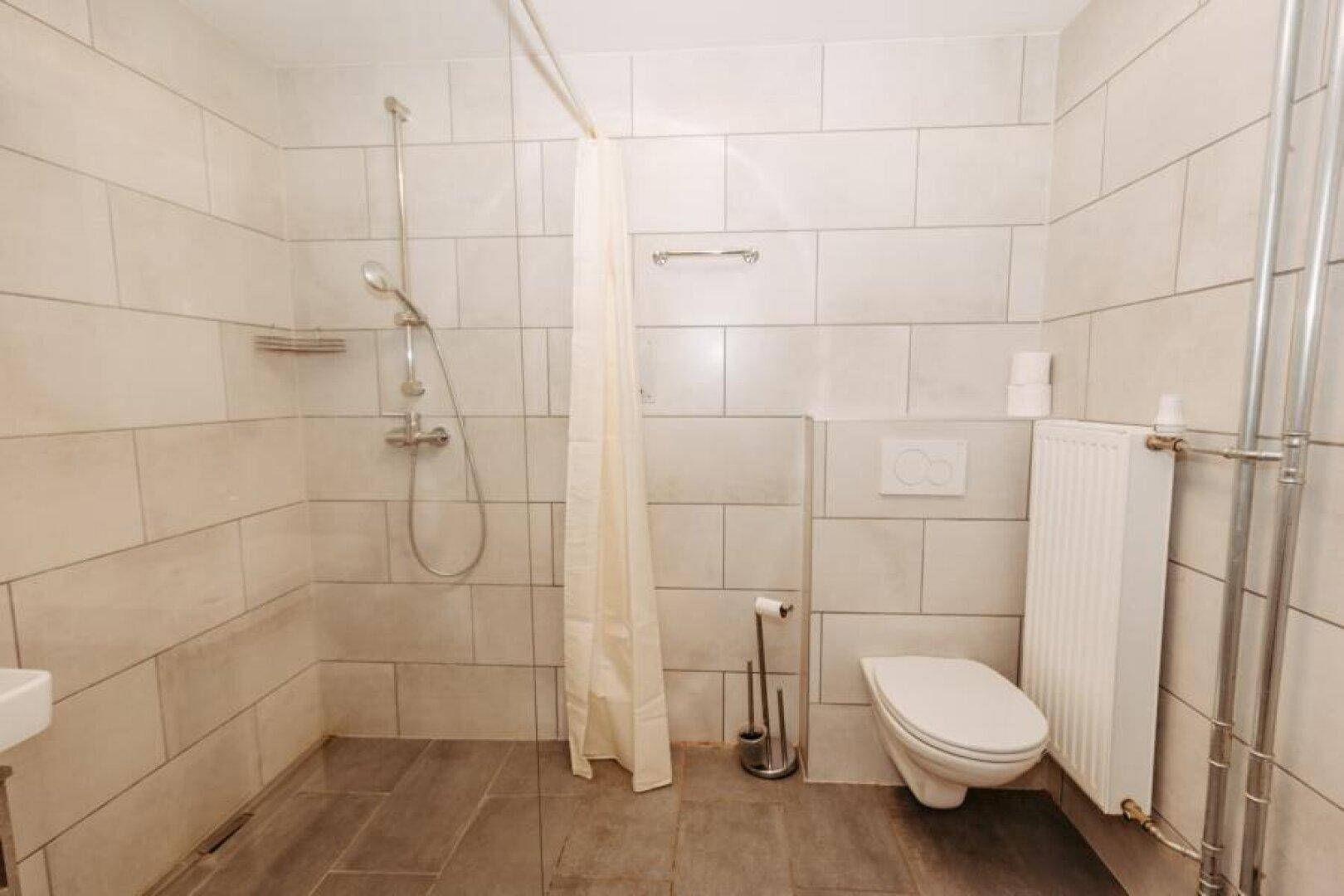 Modern gefliestes Badezimmer mit ebenerdiger Dusche und wandhängendem WC.