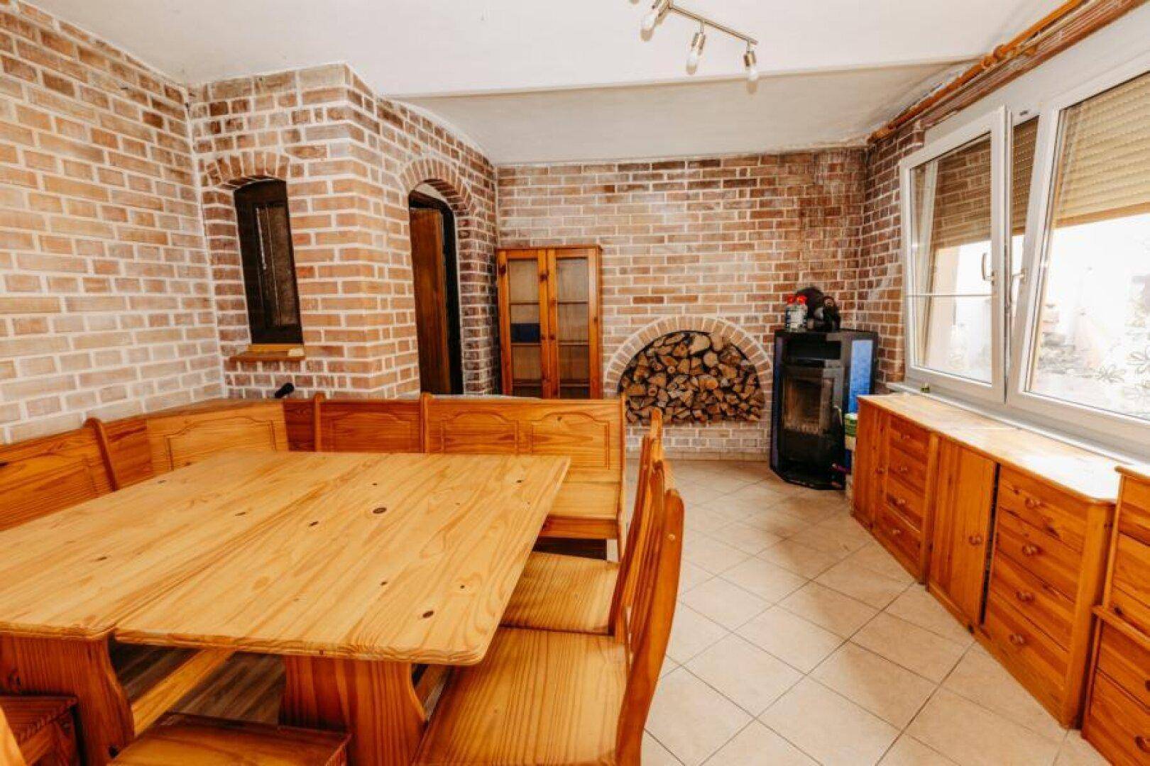 Rustikaler Essbereich mit Holztisch, Bänken und Ziegelwänden, inklusive Kaminofen.