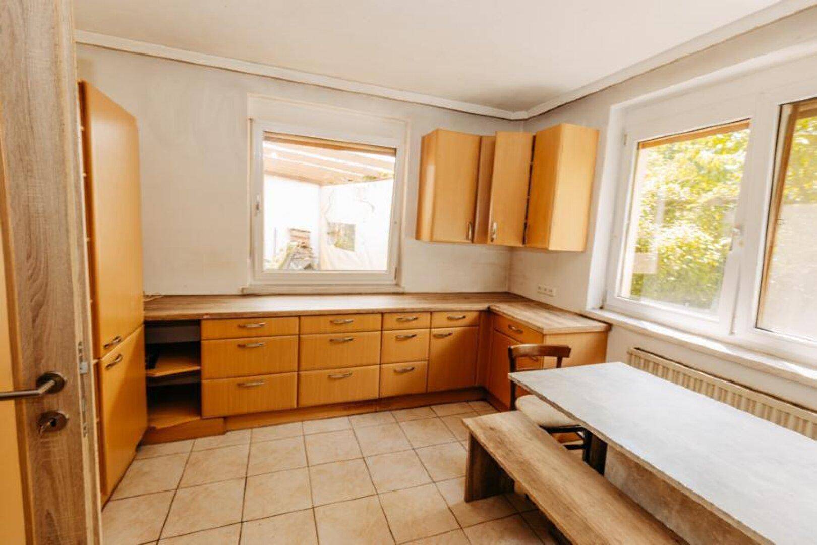 Küche mit Holzschränken, Essbereich und viel Tageslicht durch zwei Fenster.