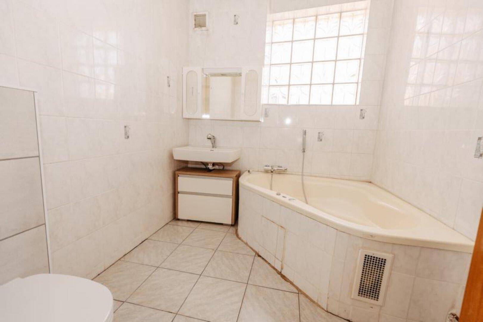 Gefliestes Badezimmer mit Eckbadewanne, Waschbecken und Spiegelschrank.