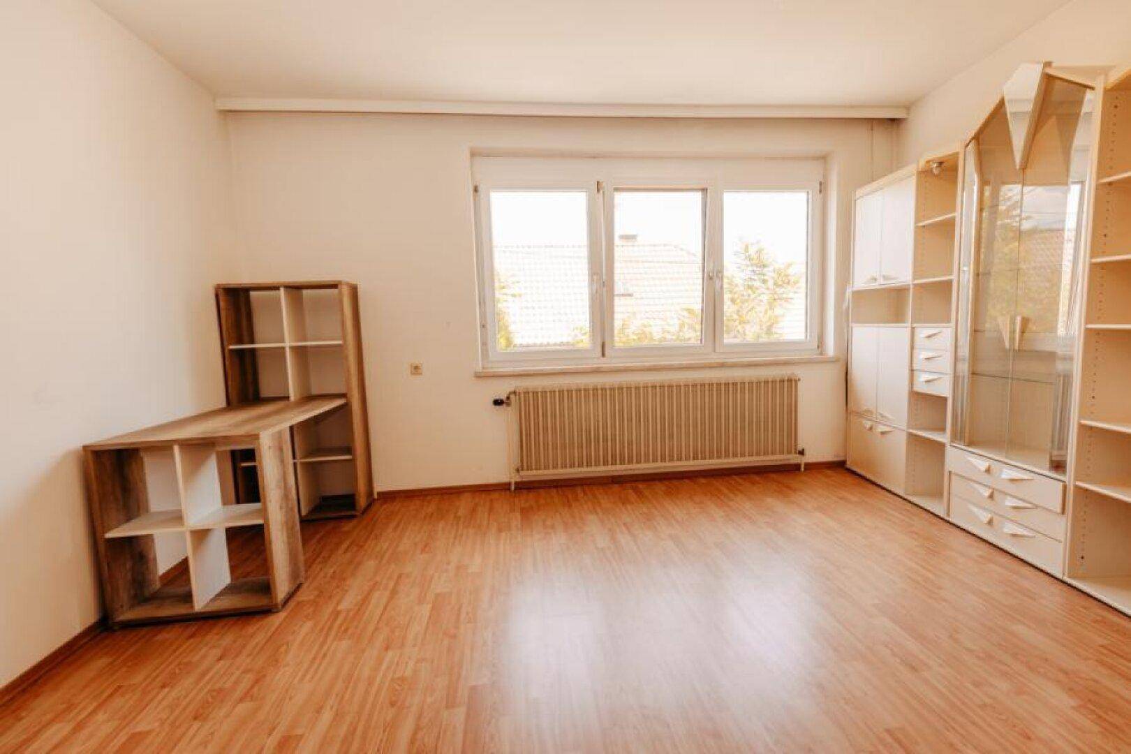 Helles Zimmer mit Laminatboden, großem Fenster und Regalsystemen.