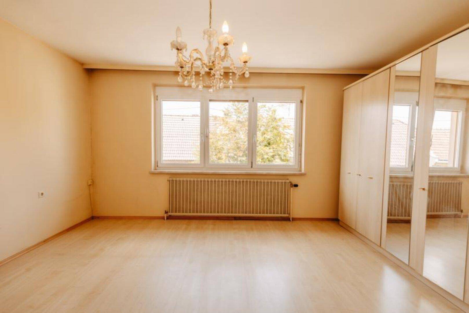 Geräumiges Schlafzimmer mit Laminatboden, großem Fenster und Kronleuchter.