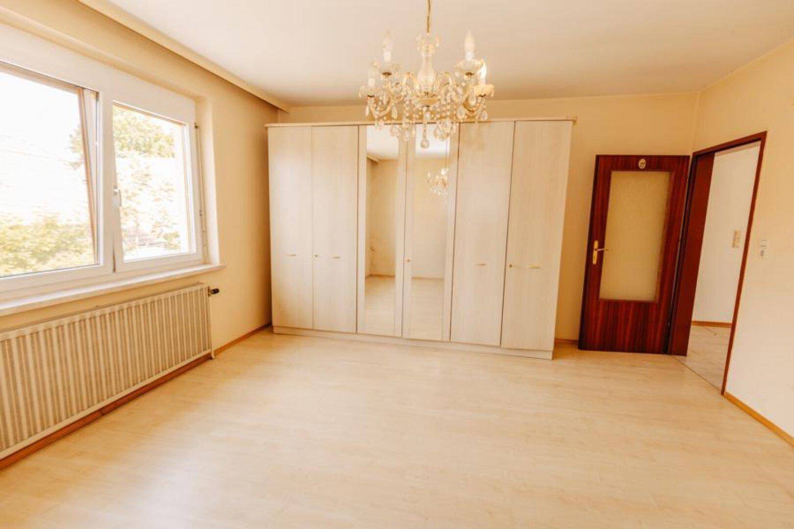Schlafzimmer mit Laminatboden, großem Fenster und einem Kleiderschrank mit Spiegeltüren.