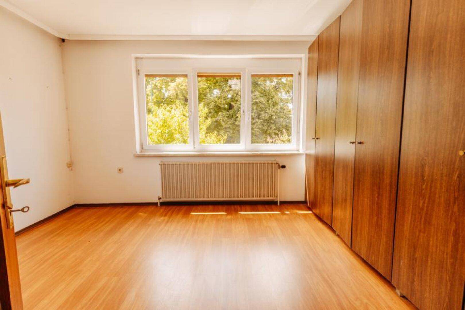 Schlafzimmer mit Laminatboden, großem Fenster und geräumigen Holzschränken.