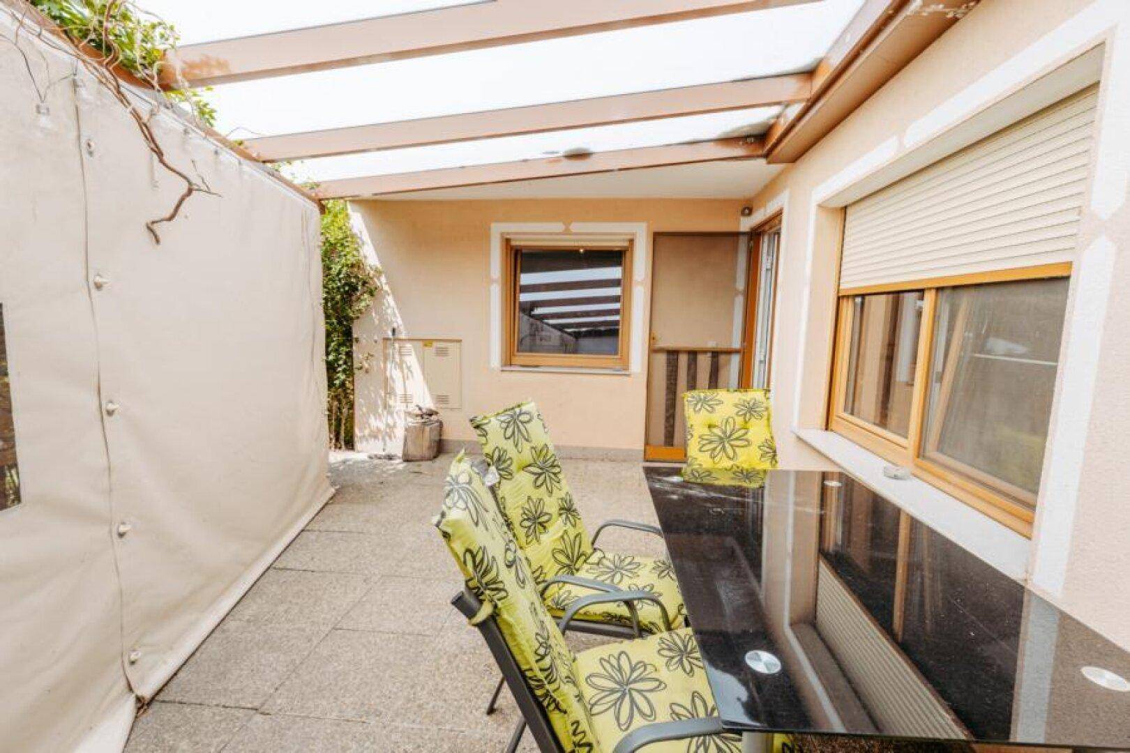 Überdachter Terrassenbereich mit Sitzgelegenheiten und Blick in den Garten.