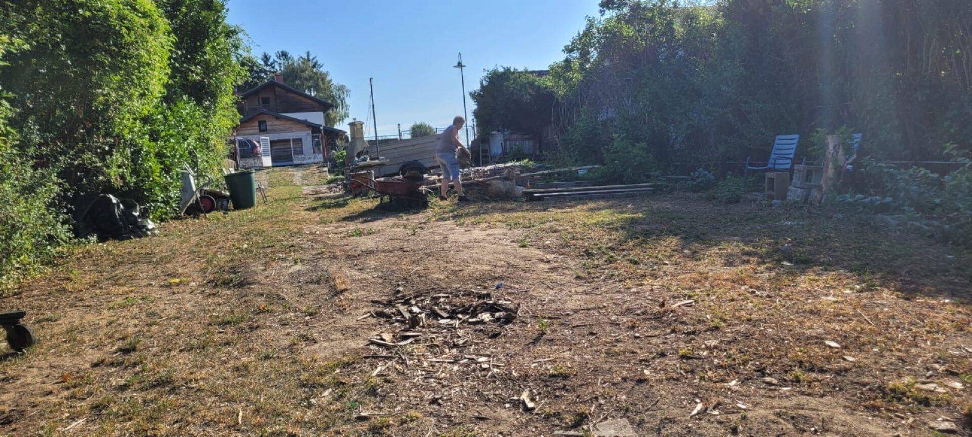Ungepflegter Gartenbereich mit einem Haus im Hintergrund und einer Person bei der Arbeit.