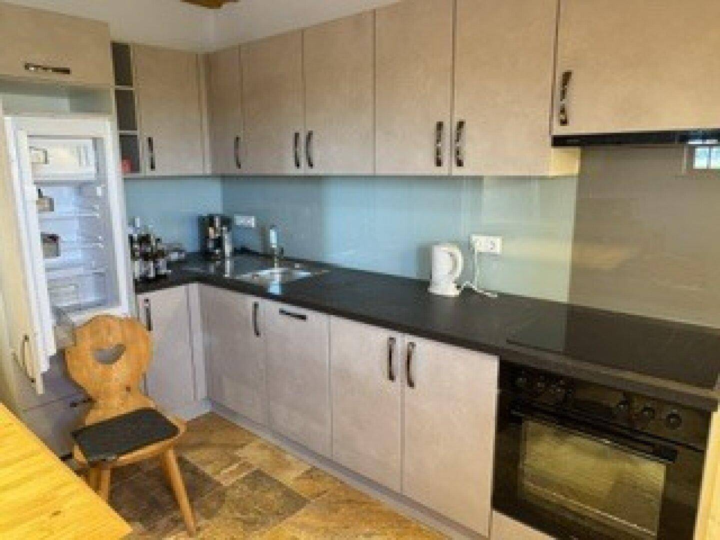 Moderne Küche mit hellgrauen Schränken, schwarzer Arbeitsplatte und integriertem Kühlschrank.