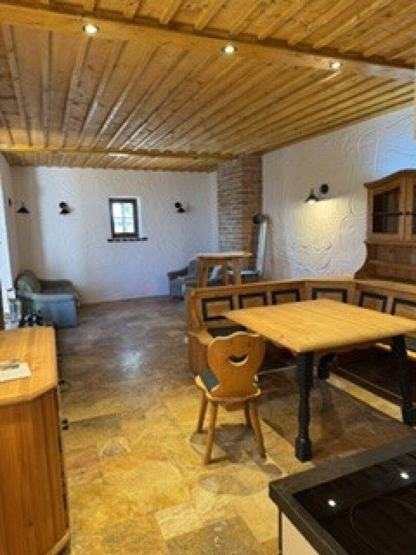 Rustikaler Wohn-Essbereich mit Holzbalkendecke, Holztisch und gefliestem Boden.
